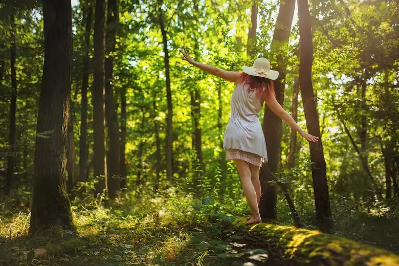 Mujer caminando sobre tronco en un bosque.